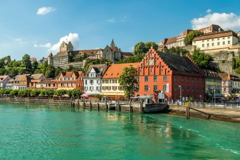 Meersburg Tourismus: malerische Altstadt mit bunten Häusern und Burg am Hang, überragt von grünen Hügeln, am glitzernden Bodensee.