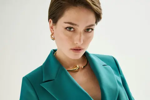 Donna con taglio pixie lungo, indossa blazer verde acqua e collana dorata.