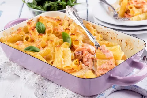 Zapiekanka z makaronem i łososiem w fioletowym naczyniu, udekorowana bazylią.