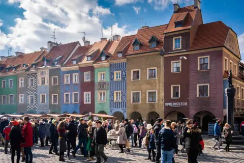 Kolorowe kamienice na Starym Rynku w Poznaniu. Tłum ludzi spaceruje po bruku. Idealne miejsce, by poczuć atmosferę miasta, gdy już wiesz, jak dojechać z dworca głównego w Poznaniu na stary rynek.