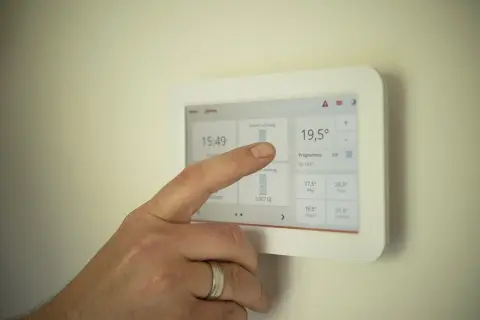 Palec dotyka ekranu termostatu, który pokazuje temperaturę 19,5°C. To nowoczesne urządzenie, które może być częścią systemu z kotłem kondensacyjnym.