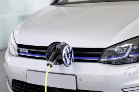 Une Golf 7 GTE blanche est branchée à une borne de recharge. Le câble jaune est visible.