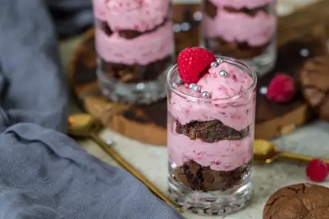 Ljuvlig hallonmousse till tårta i glas, varvad med chokladkaka och toppad med färsk hallon och silverkulor.