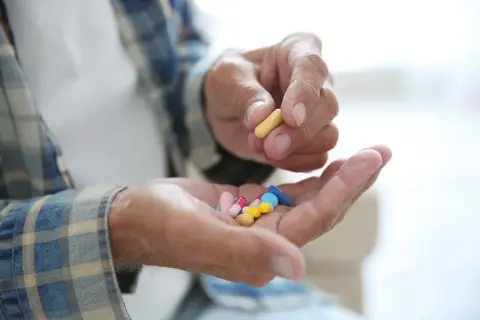 Dłoń starszego mężczyzny trzyma garść kolorowych tabletek, jedną żółtą kapsułkę, być może inhibitory MAO.