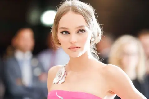 Lily-Rose Depp, con un vestido rosa y maquillaje dramático, posa con elegancia.