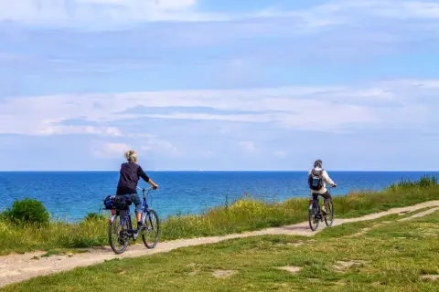 Dwie osoby jadą rowerami po malowniczej nadmorskiej trasie rowerowej. Piękne błękitne niebo i morze.