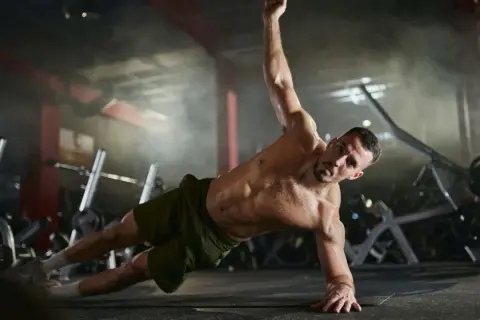 Mann trainiert seine **abs muskeln** in einem Fitnessstudio. Er macht eine seitliche Plank-Übung, wobei sein Körper gerade und angespannt ist.