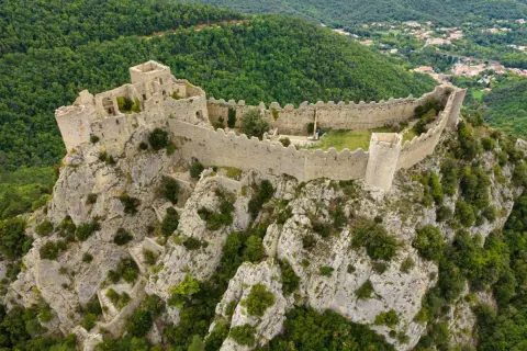 Vestiges d'un château abandonné en Occitanie, perché sur un éperon rocheux, dominant une vallée verdoyante.