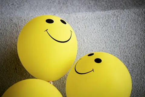 Żółte balony ze śmiejącymi się buźkami, symbolizujące pozytywną kulturę feedbacku i otwartą komunikację.