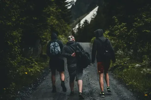 Tres amigos caminan por un sendero boscoso, una aventura perfecta para conocer gente y disfrutar de la naturaleza.
