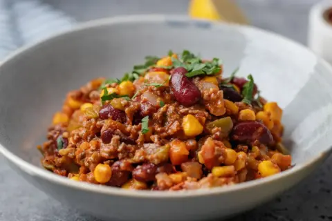 Miseczka pełna aromatycznego chili con carne z fasolą, kukurydzą i mielonym mięsem, posypana świeżą natką pietruszki.