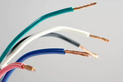 Pięć przewodów elektrycznych w różnych kolorach: zielonym, białym, czarnym, niebieskim i różowym, odsłaniających miedziane żyły. Różnorodność kolorów faz ułatwia identyfikację.