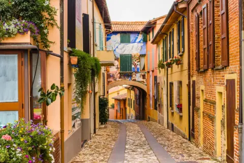 Un vicolo pittoresco tra i borghi medievali dell'Emilia Romagna, con case colorate, fiori e murales vivaci.