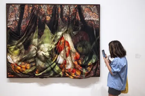 A woman photographs a draped artwork featuring fruits and vegetables, made in LA Hammer.