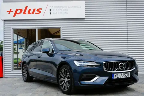 Ciemnoniebieskie Volvo V60 Hybrid z polskimi tablicami WL 7253Y przed budynkiem z logo "+plus".