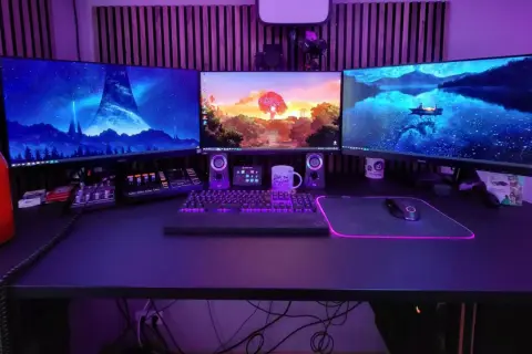 Ein episches **gaming set up** mit drei Monitoren, beleuchteter Tastatur und Maus. Im Hintergrund leuchtet lila Beleuchtung.