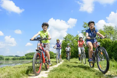 Familie genießt das **Radfahren mit Kindern** auf einem sonnigen Weg am See.