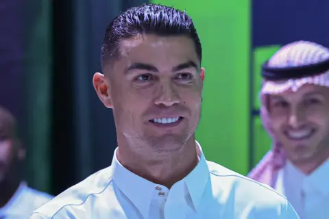 Cristiano Ronaldo w białej koszuli, uśmiecha się. W tle mężczyzna w tradycyjnym arabskim stroju.