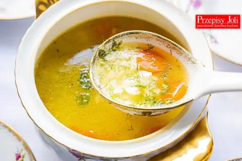 A ladle lifts a spoonful of the **najlepsza zupa ryżowa**, revealing tender rice, carrots, and dill in a golden broth.