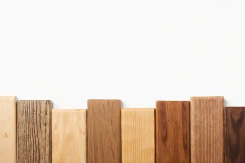 Bloques de madera dura de diferentes tonos y texturas, dispuestos en fila sobre fondo blanco.