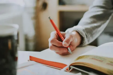 Mano escribiendo en un cuaderno con ejercicios de tiempos verbales en español.