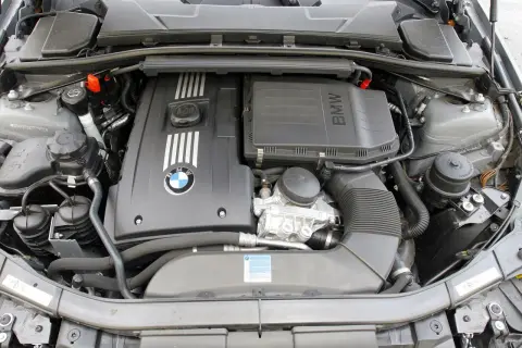 Silnik BMW E90. Widoczny jest czarny, plastikowy kolektor dolotowy, pokrywa silnika z logo BMW i oznaczeniem M, a także zbiornik płynu chłodniczego.