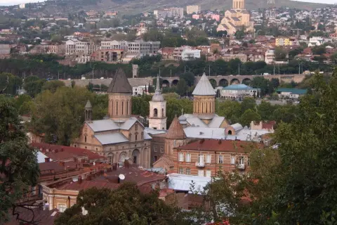 Widok na Tbilisi, gdzie zabytkowe cerkwie i domy z czerwonymi dachami opowiadają historię Gruzji. W tle widać wzgórza i nowoczesne budynki.