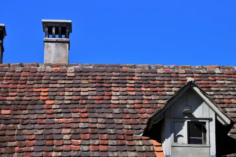 Dwa kominy na dachu pokrytym starymi dachówkami, wymagające naprawy komina z cegły.