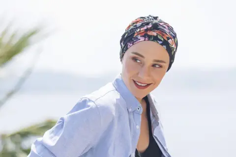 Frauen mit einem gebundenen Kopftuch, das sie während der Chemo tragen, lächeln zuversichtlich in die Kamera.