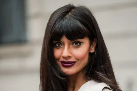 Frau mit stufig langen Haaren mit Pony, dunklem Lippenstift und auffälligem Augen-Make-up.
