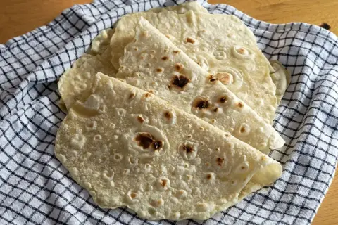 Świeżo upieczone placki na tortilla przepis, ułożone na kratkowanej ściereczce. Idealne do wrapów i quesadilli.