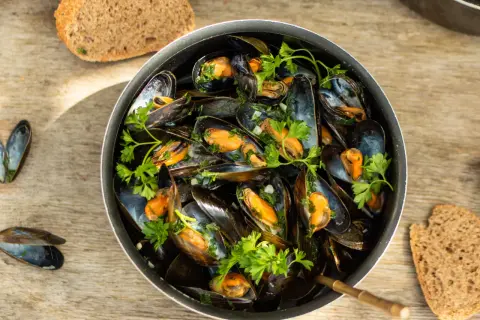 Un plat généreux de moules marinières, garni de persil frais, servi avec du pain de campagne sur une table en bois.