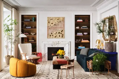 A living room showcasing how to mix modern and vintage decor with a plush yellow armchair, ornate mirror, and a marble fireplace.