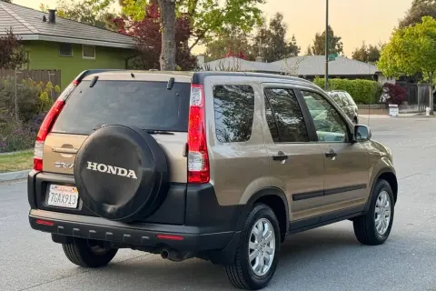 En gyllene Honda CRV 2005 står parkerad på en gata, med reservhjulet synligt på bakluckan.