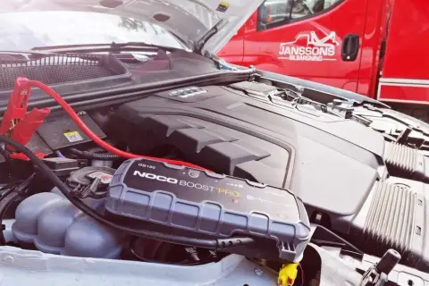 Bil startar inte kallt ute. Startkablar och en batteriboost kopplade till bilens motor.