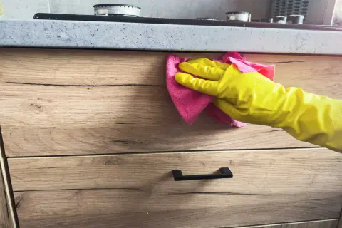 Main jaune essuyant une tache sur bois avec un chiffon rose.