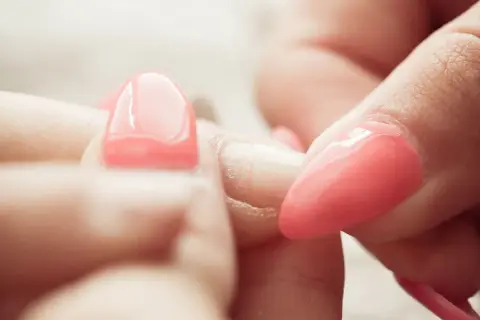 Zbliżenie na dłonie, gdzie widać proces usuwania manicure tytanowego. Różowe paznokcie są w trakcie zdejmowania.