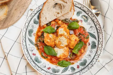 En tallrik med ricotta recept: smakliga ricotta-bollar i tomatsås med kikärtor, spenat och basilika, serverad med rostat bröd.