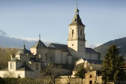 El imponente monasterio del Paular se alza bajo un cielo azul, con sus cúpulas y campanario de piedra bañados por el sol.