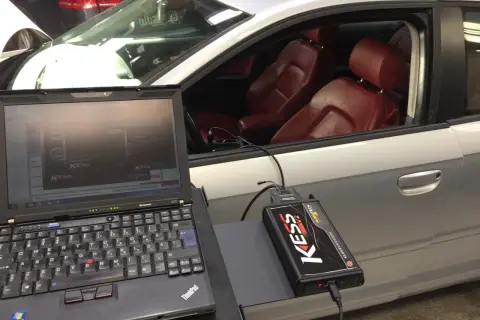 Laptop och KESS-enhet kopplade till en bil för att chippa bilen. Röd läderinredning syns i kupén.