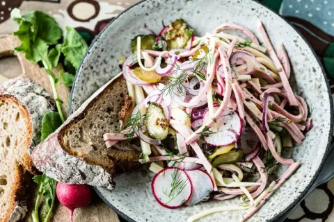 Ein bayerischer Wurstsalat, garniert mit Radieschen, Zwiebeln und Dill, serviert mit Bauernbrot.