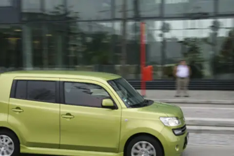 Zielony Daihatsu Materia jedzie ulicą obok nowoczesnego budynku.