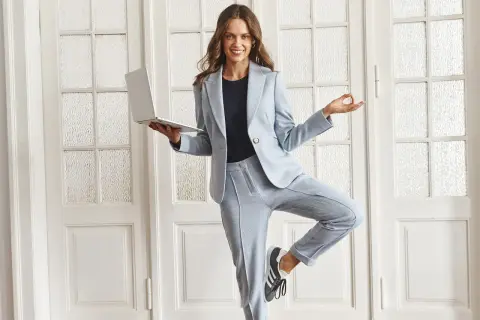 Kobieta w jasnoniebieskim garniturze i sneakersach, trzymająca laptopa, w pozie jogi. Idealny casual style damski do pracy i relaksu.