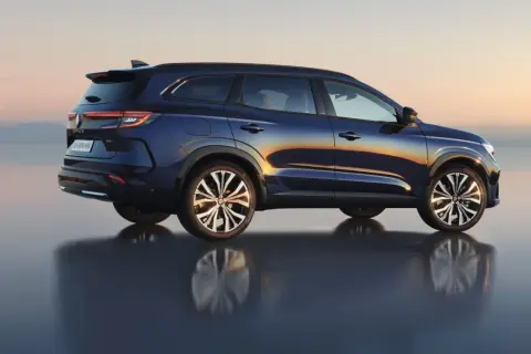 Granatowy Renault Espace 2024 z odbiciem na wodzie, na tle zachodzącego słońca.