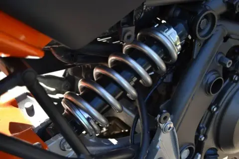 Gros plan sur l'amortisseur d'une moto, avec son ressort argenté et son corps noir. Une légère fuite d'amortisseur est visible, nécessitant une réparation.