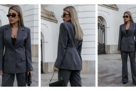 Elegancka kobieta w szarym garniturze, prezentująca styl minimalistyczny ubiór. Czarna koronkowa bluzka i okulary dodają charakteru.