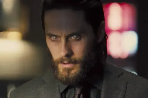 Jared Leto w filmach, z bladymi oczami i brodą, w garniturze.