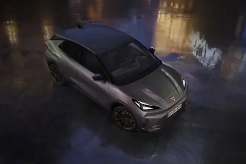 Nowoczesny Cupra Raval w ciemnoszarym kolorze, z czarnym dachem, stoi na mokrej nawierzchni, odbijając światła miasta.