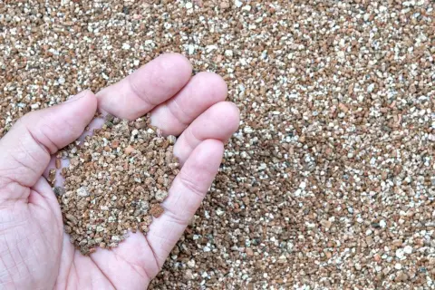 Main d'une personne tenant une poignée de vermiculite, un matériau léger et poreux. Sa composition est idéale pour l'horticulture.