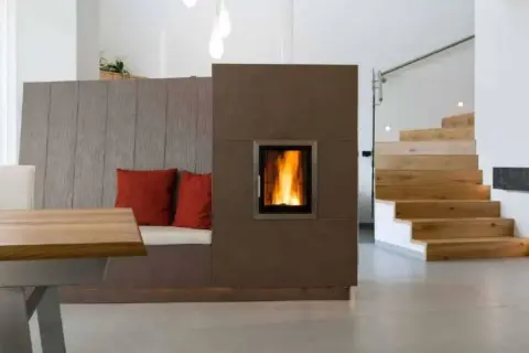 Moderner Wohnraum mit gemütlicher Sitzbank, Kamin und Holztreppe. Die Pelletheizung im Kamin sorgt für Wärme, die Vorschriften sind eingehalten.